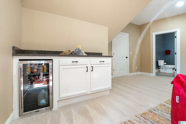 bar with wine cooler, white cabinetry, dark stone countertops, and light carpet