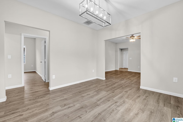 empty room with light hardwood / wood-style floors and ceiling fan with notable chandelier