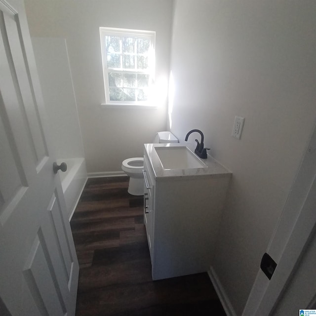 bathroom featuring wood-type flooring, vanity, a tub to relax in, and toilet