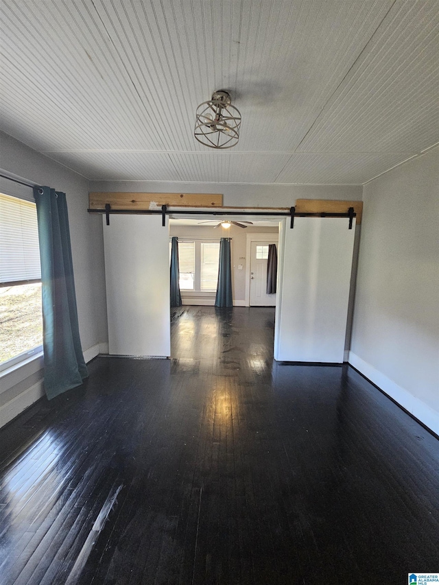 empty room with a barn door and dark hardwood / wood-style floors