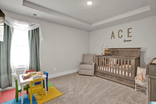 bedroom with a crib, carpet, a tray ceiling, and multiple windows