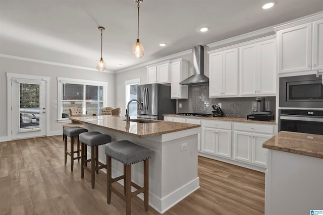 kitchen featuring white cabinets, wall chimney exhaust hood, an island with sink, and appliances with stainless steel finishes