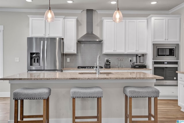 kitchen with white cabinets, wall chimney range hood, light stone countertops, an island with sink, and stainless steel appliances