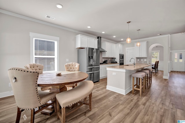 kitchen with white cabinets, hanging light fixtures, light stone countertops, an island with sink, and stainless steel appliances