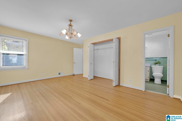 unfurnished bedroom featuring a notable chandelier, light hardwood / wood-style floors, ensuite bathroom, and tile walls