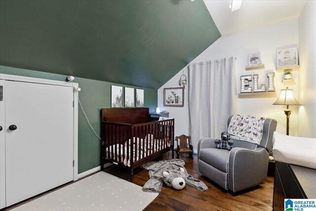 bedroom featuring hardwood / wood-style flooring, a nursery area, and lofted ceiling