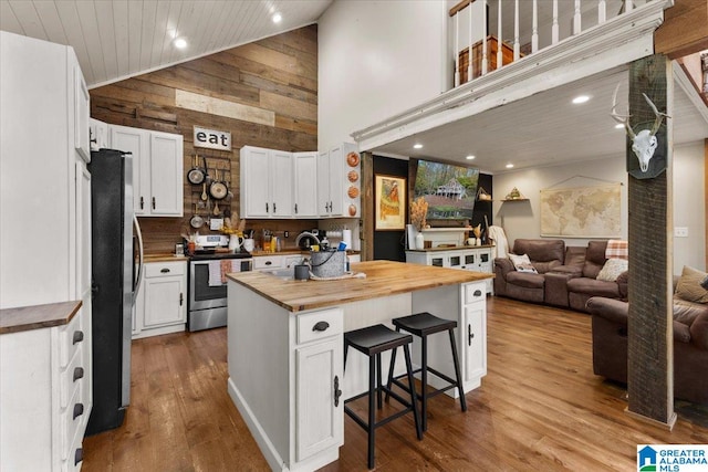 kitchen with white cabinetry, wood counters, high vaulted ceiling, wooden walls, and appliances with stainless steel finishes