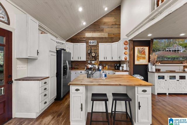 kitchen with wood counters, stainless steel fridge, wooden walls, a center island, and white cabinetry