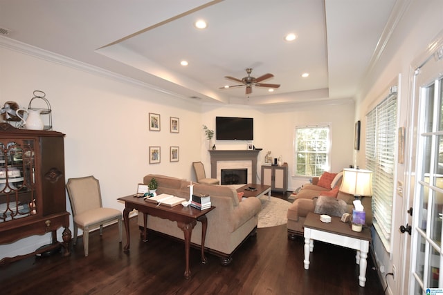 living room featuring a tray ceiling, ceiling fan, dark wood-type flooring, and ornamental molding