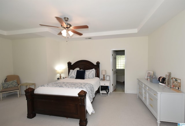 bedroom with a raised ceiling, ensuite bath, ceiling fan, and light carpet