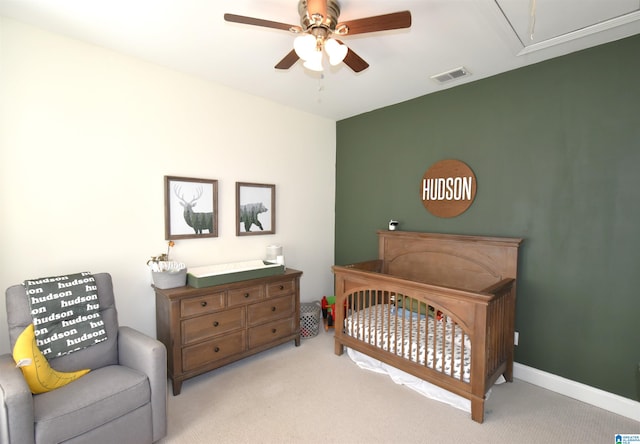 bedroom with a crib, light carpet, and ceiling fan