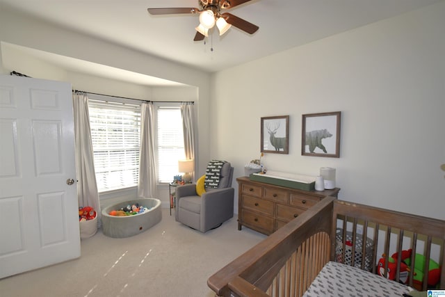 bedroom with light carpet, ceiling fan, and a nursery area