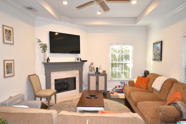 living room with a raised ceiling, ceiling fan, crown molding, and a fireplace