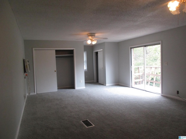 unfurnished bedroom featuring ceiling fan, carpet floors, a textured ceiling, and multiple closets