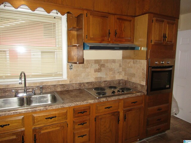 825 Goldwire St SW, Birmingham, AL 35211 - kitchen featuring stainless steel appliances, under cabinet range hood, a sink, brown cabinetry, and decorative backsplash