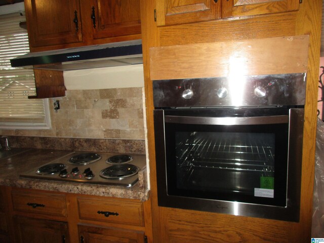 825 Goldwire St SW, Birmingham, AL 35211 - kitchen view of under cabinet range hood, stainless steel electric cooktop, oven, brown cabinets, and tasteful backsplash