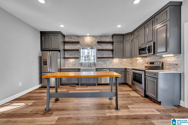 kitchen with appliances with stainless steel finishes, backsplash, light hardwood / wood-style floors, and gray cabinetry