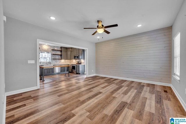 unfurnished living room featuring ceiling fan, light hardwood / wood-style flooring, wooden walls, and sink