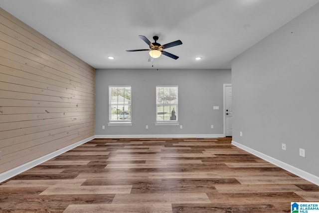 empty room with hardwood / wood-style flooring, ceiling fan, and wood walls