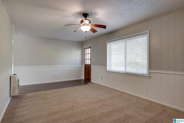 carpeted spare room featuring ceiling fan, wood walls, and a textured ceiling