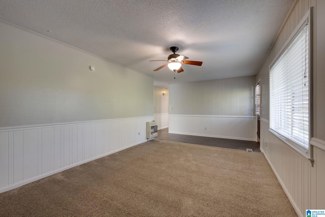 empty room featuring carpet flooring, heating unit, ceiling fan, and a textured ceiling