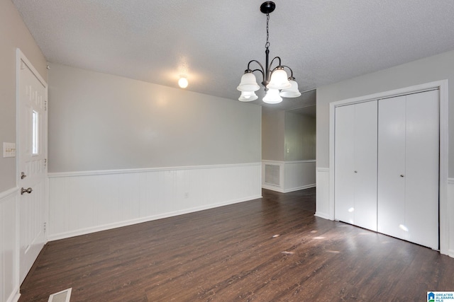 unfurnished dining area featuring dark wood-type flooring, a textured ceiling, and a notable chandelier