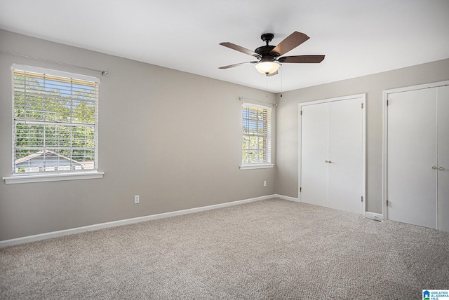 unfurnished bedroom featuring two closets, ceiling fan, and carpet