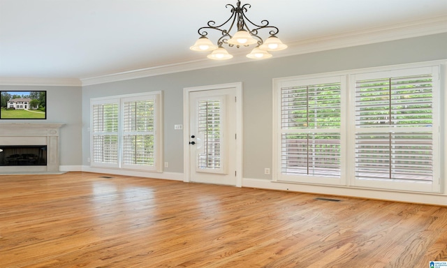 unfurnished living room featuring plenty of natural light, light wood-type flooring, ornamental molding, and an inviting chandelier