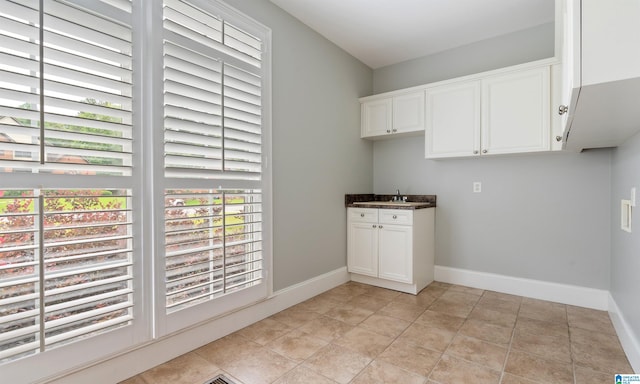 laundry area featuring sink, light tile patterned floors, and cabinets