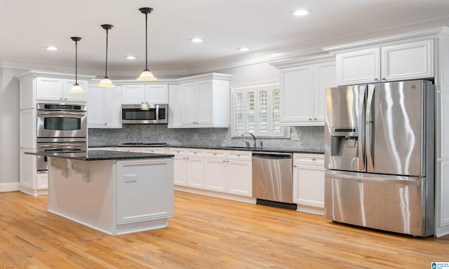 kitchen with white cabinets, appliances with stainless steel finishes, decorative light fixtures, and light hardwood / wood-style flooring