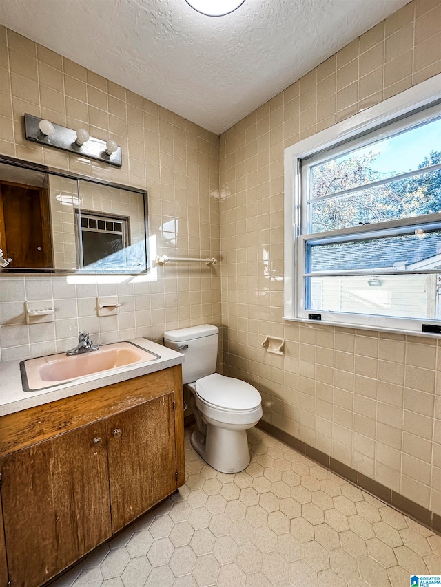 bathroom with tile patterned floors, vanity, a textured ceiling, tile walls, and toilet