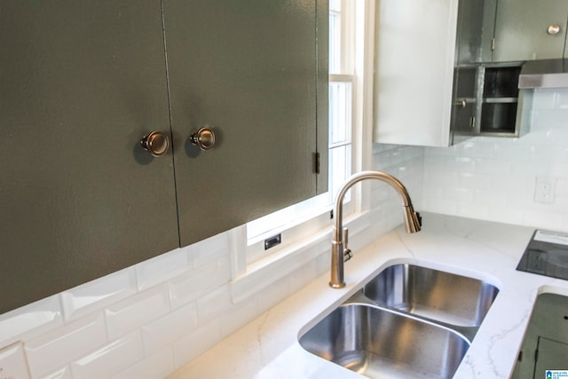 interior details with backsplash, sink, green cabinetry, range hood, and light stone counters