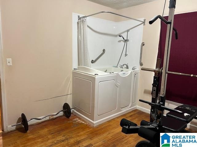 exercise room featuring washer / clothes dryer, hardwood / wood-style floors, and a textured ceiling