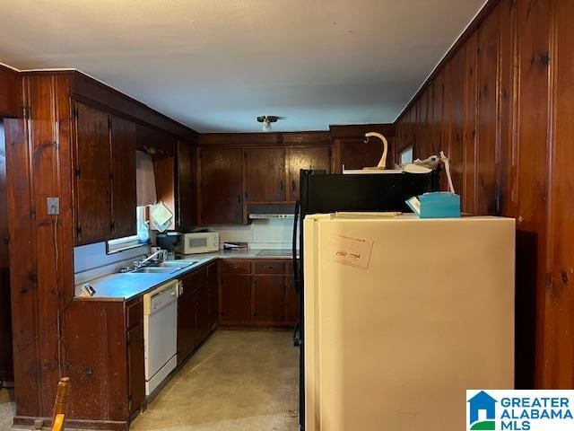 kitchen with white appliances, sink, and wood walls