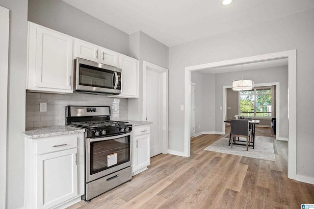 kitchen with light wood-type flooring, backsplash, light stone counters, stainless steel appliances, and white cabinetry