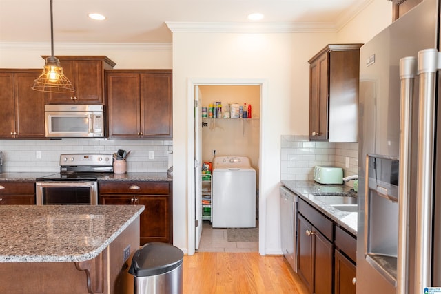 kitchen with pendant lighting, sink, light wood-type flooring, stainless steel appliances, and washer / clothes dryer