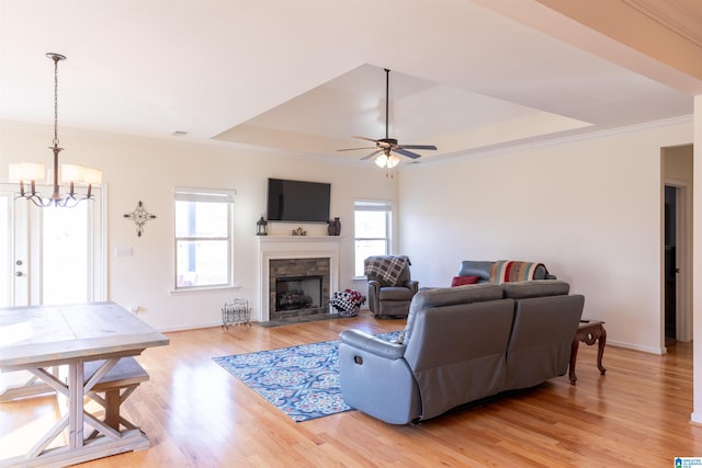 living room featuring a raised ceiling, crown molding, a healthy amount of sunlight, and light wood-type flooring