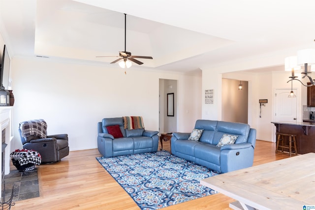 living room with hardwood / wood-style flooring, ceiling fan, ornamental molding, and a tray ceiling