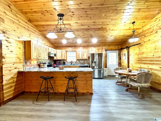 kitchen featuring kitchen peninsula, stainless steel appliances, a barn door, hardwood / wood-style floors, and wood walls