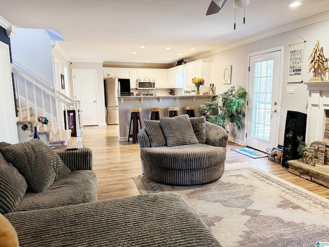 living room with a fireplace, light hardwood / wood-style flooring, ceiling fan, and ornamental molding