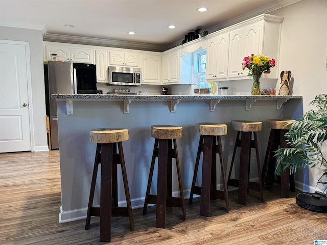 kitchen featuring light wood-type flooring, stainless steel appliances, white cabinetry, and ornamental molding