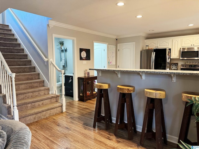 kitchen with white cabinetry, light hardwood / wood-style floors, a kitchen bar, appliances with stainless steel finishes, and ornamental molding