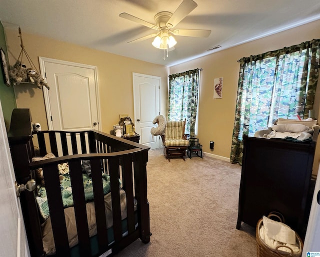 carpeted bedroom featuring ceiling fan and a nursery area