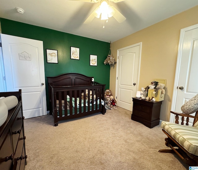 carpeted bedroom featuring ceiling fan and a nursery area