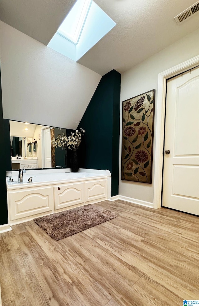 bathroom with vaulted ceiling with skylight and wood-type flooring