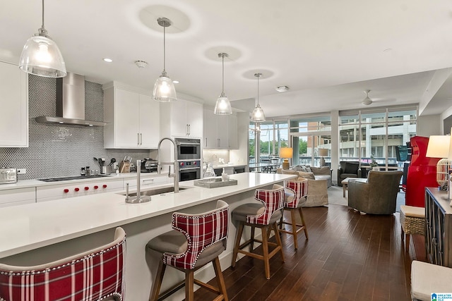 kitchen with a breakfast bar, dark wood-type flooring, wall chimney range hood, decorative light fixtures, and white cabinets