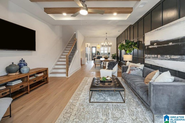 living room with ceiling fan with notable chandelier, light wood-type flooring, and a tray ceiling