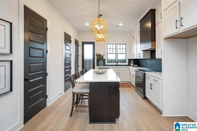 kitchen with light wood-type flooring, a kitchen island, pendant lighting, white cabinetry, and stainless steel electric range