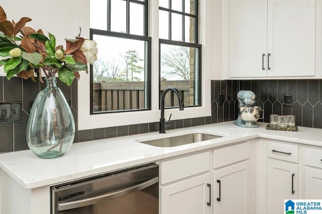 kitchen featuring decorative backsplash, white cabinets, light stone counters, sink, and dishwasher