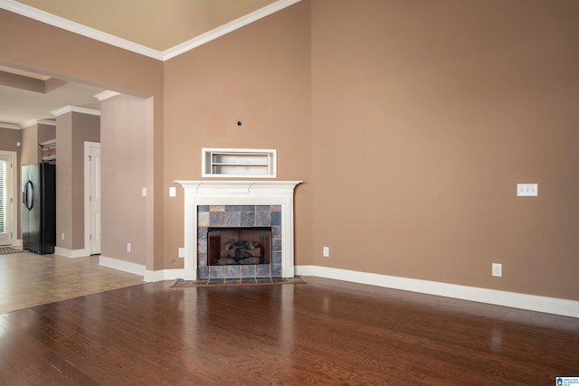 unfurnished living room with wood-type flooring, ornamental molding, and a tiled fireplace